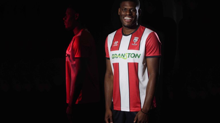 Chris Vaughan Photography - commercial photography | An image of Lincoln City’s TJ Eyoma modelling a clubs red and white shirt. The image is shot against a black background and features a multiple exposure with a side on image of TJ illuminated in red lighting.