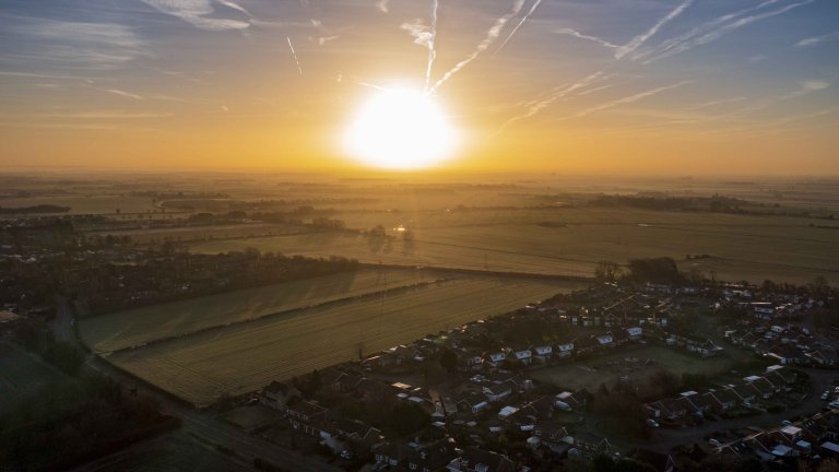 Chris Vaughan Photography - drone images | An aerial image of a sunrise over a housing area surrounded by fields.
