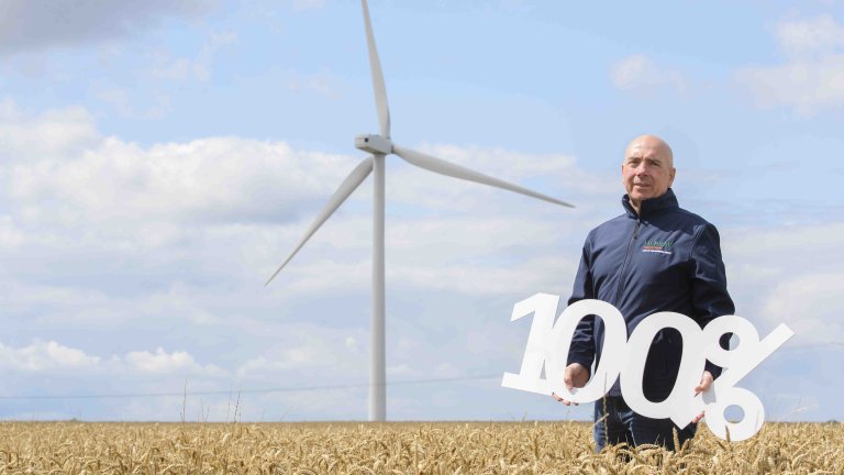 Chris Vaughan Photography - PR and communications images | A man holds a sign reading 100%, promoting renewable energy, in front of a wind turbine.