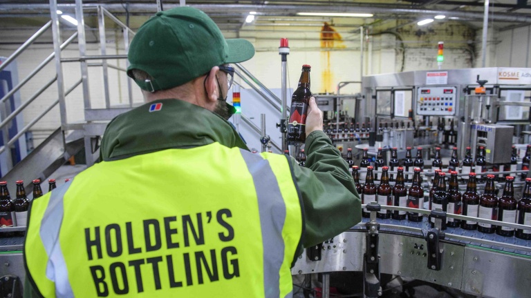 Chris Vaughan Photography - Commercial images | A member of staff inspects the label on a bottle of beer. He is wearing a high-vis jacket with the company name on it.