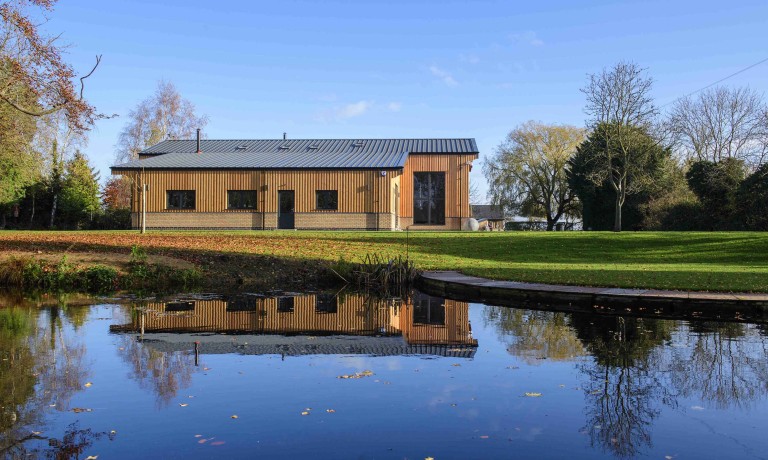 Chris Vaughan Photography - commercial images | A barn conversion photographed across a lake which reflects part of the building.