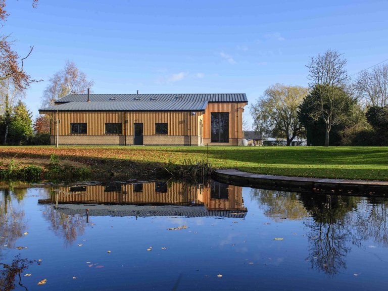 Chris Vaughan Photography - commercial images | A barn conversion photographed across a lake which reflects part of the building.