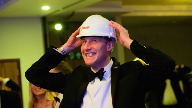 Chris Vaughan Photography - corporate event images | A contestant, wearing a hard hat promoting one of the event's sponsors, puts his hands on his head during an ice-breaker game of heads and tails at an awards ceremony.