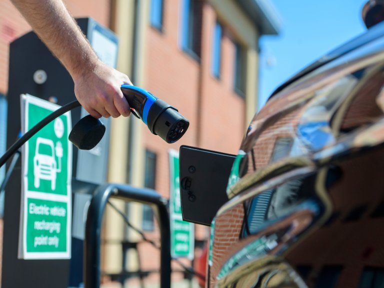 A hand prepares to connect an electric vehicle to a car charger.